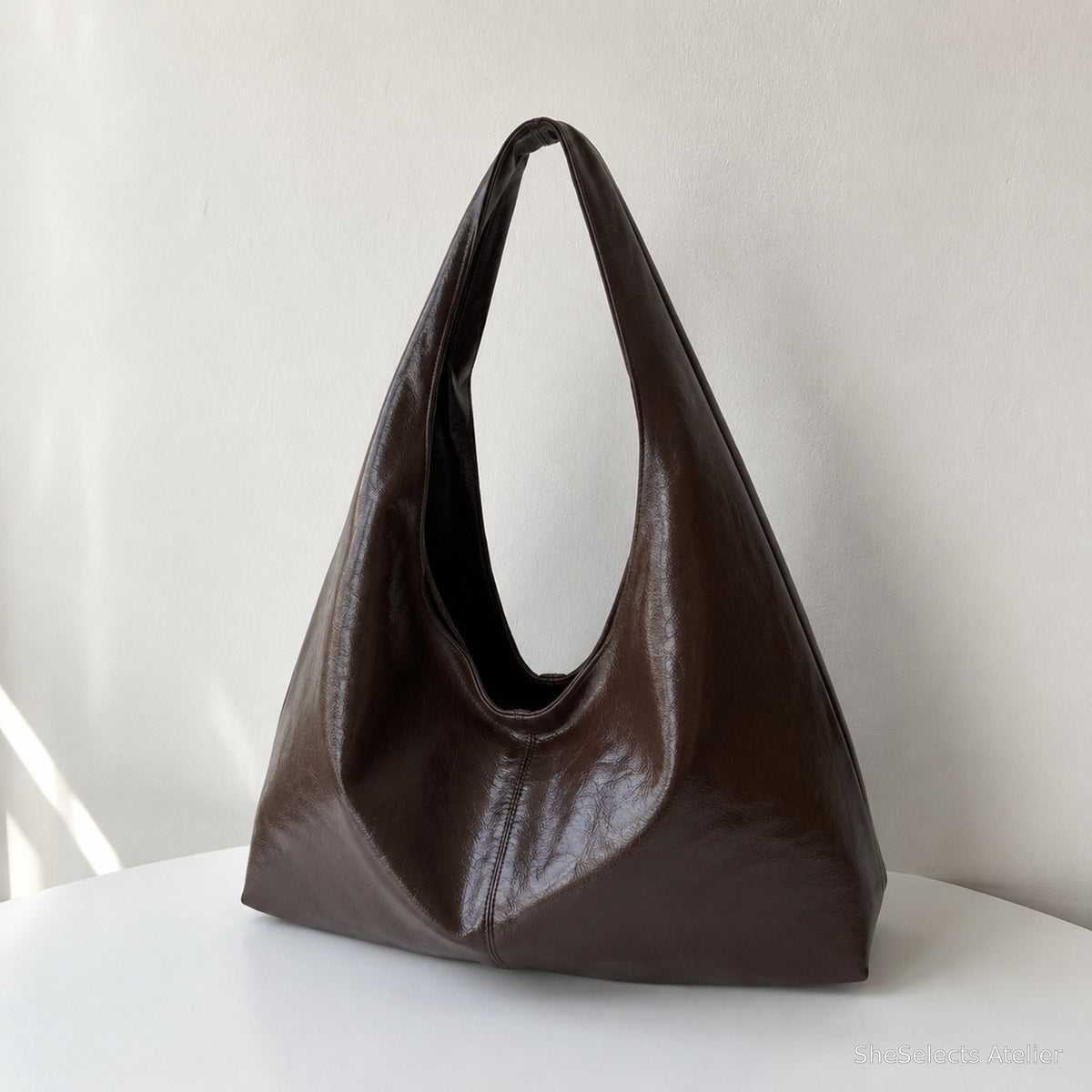 Coffee brown slouchy vegan leather hobo bag on a white table in natural window light