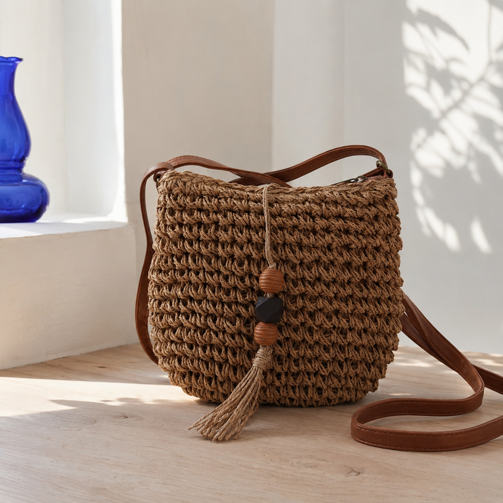 Brown woven straw crossbody bag with beaded tassel on pale oak