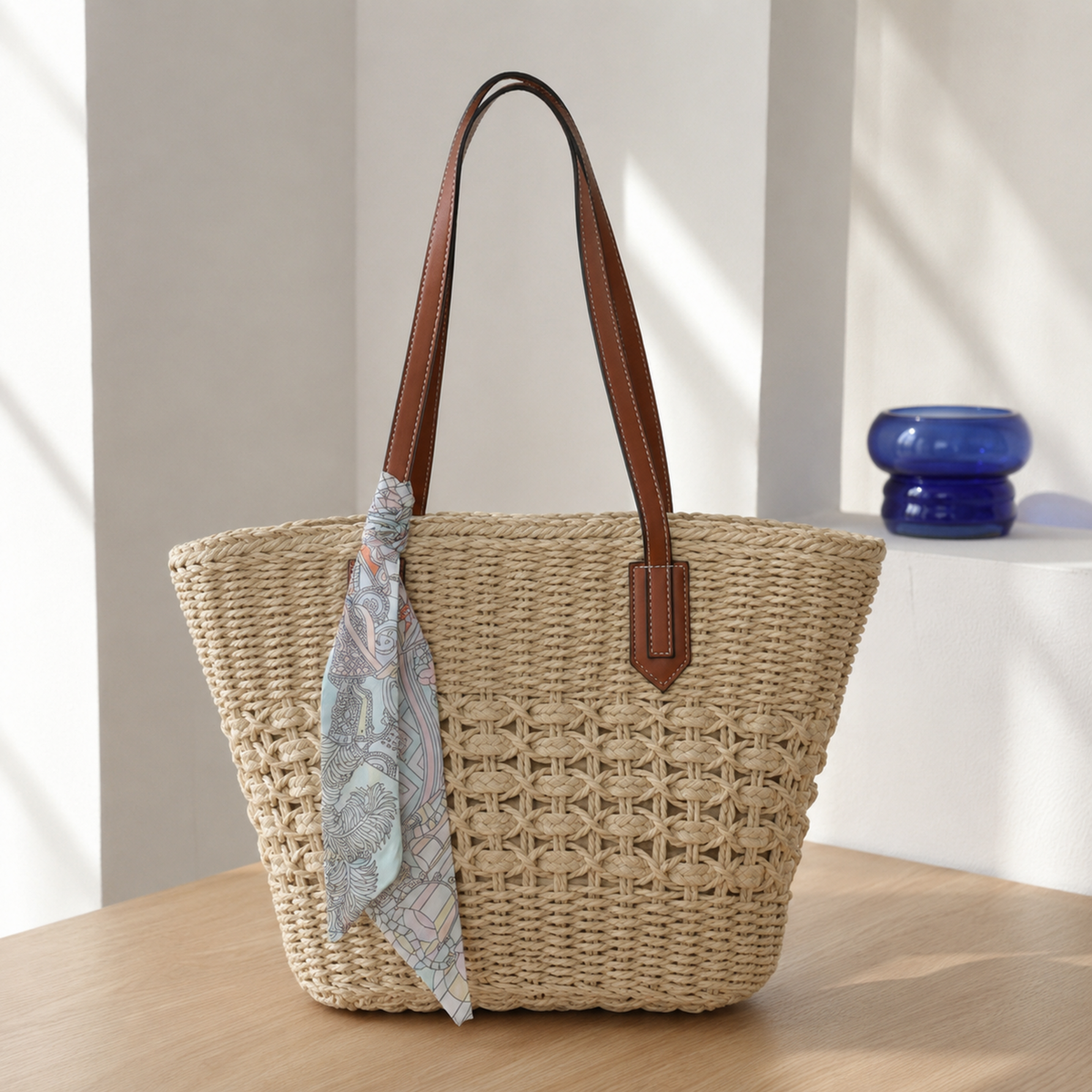 Beige cut-out woven paper-straw tote with patterned scarf in soft daylight