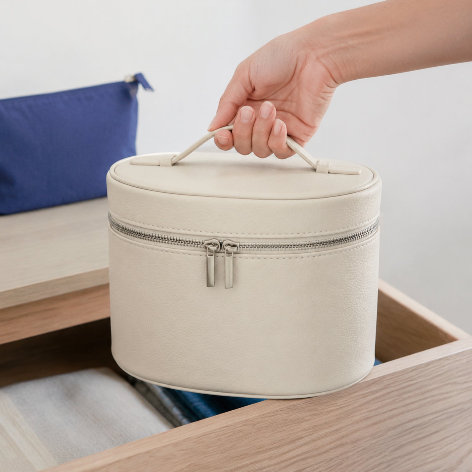 Beige oval makeup organizer carried by its short top handle above a pale oak drawer