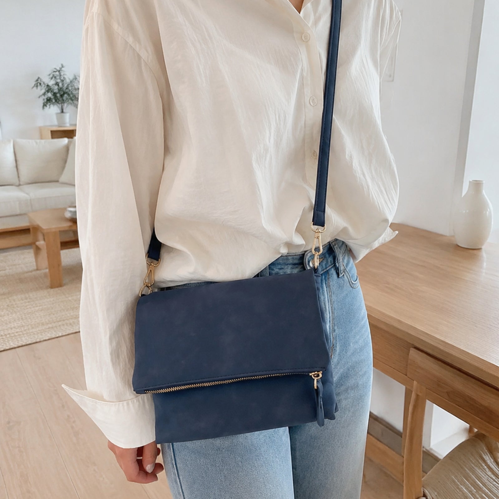 Navy blue envelope crossbody worn with an ivory shirt and light denim in a bright home