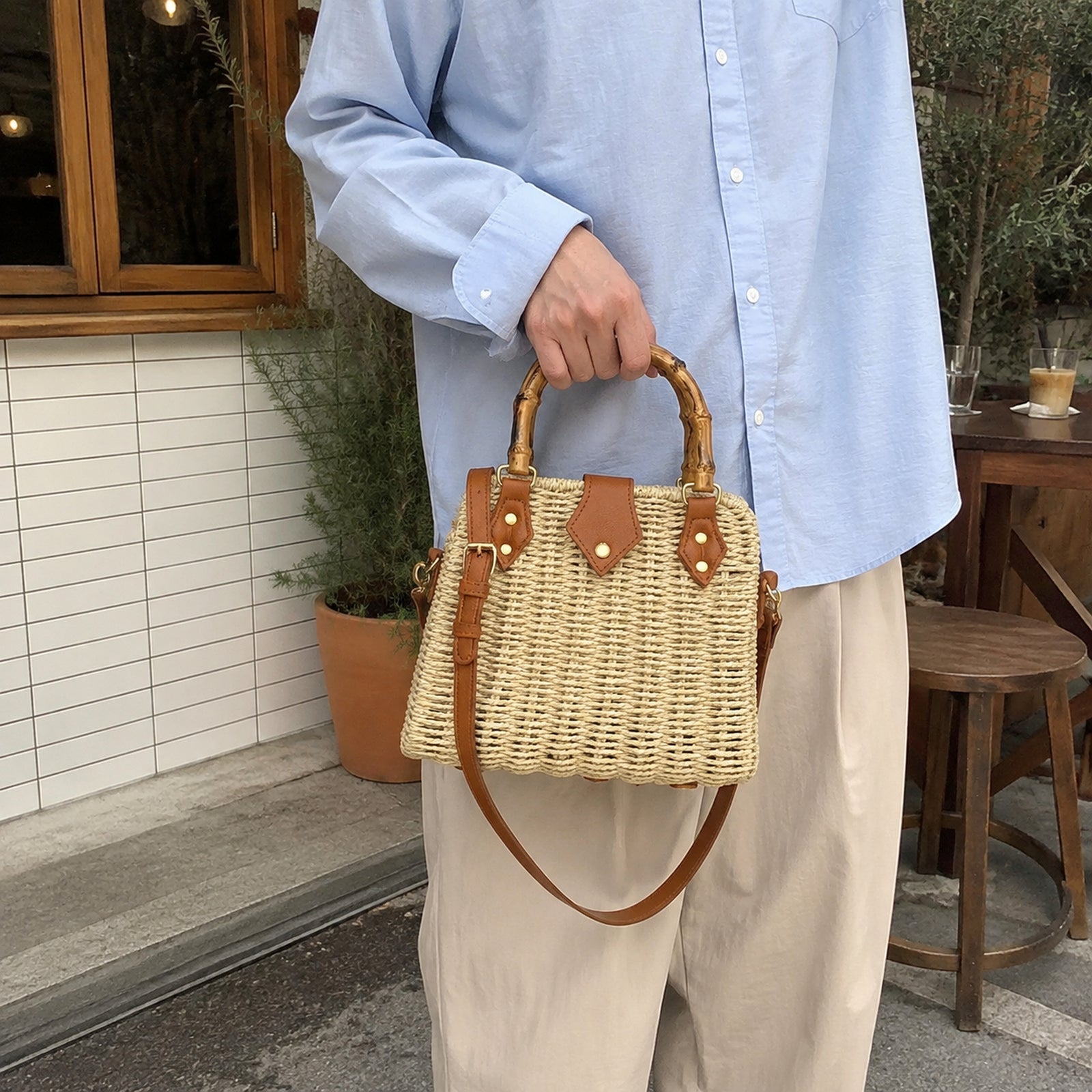 Structured woven bamboo handle bag carried by hand with a blue shirt and neutral trousers