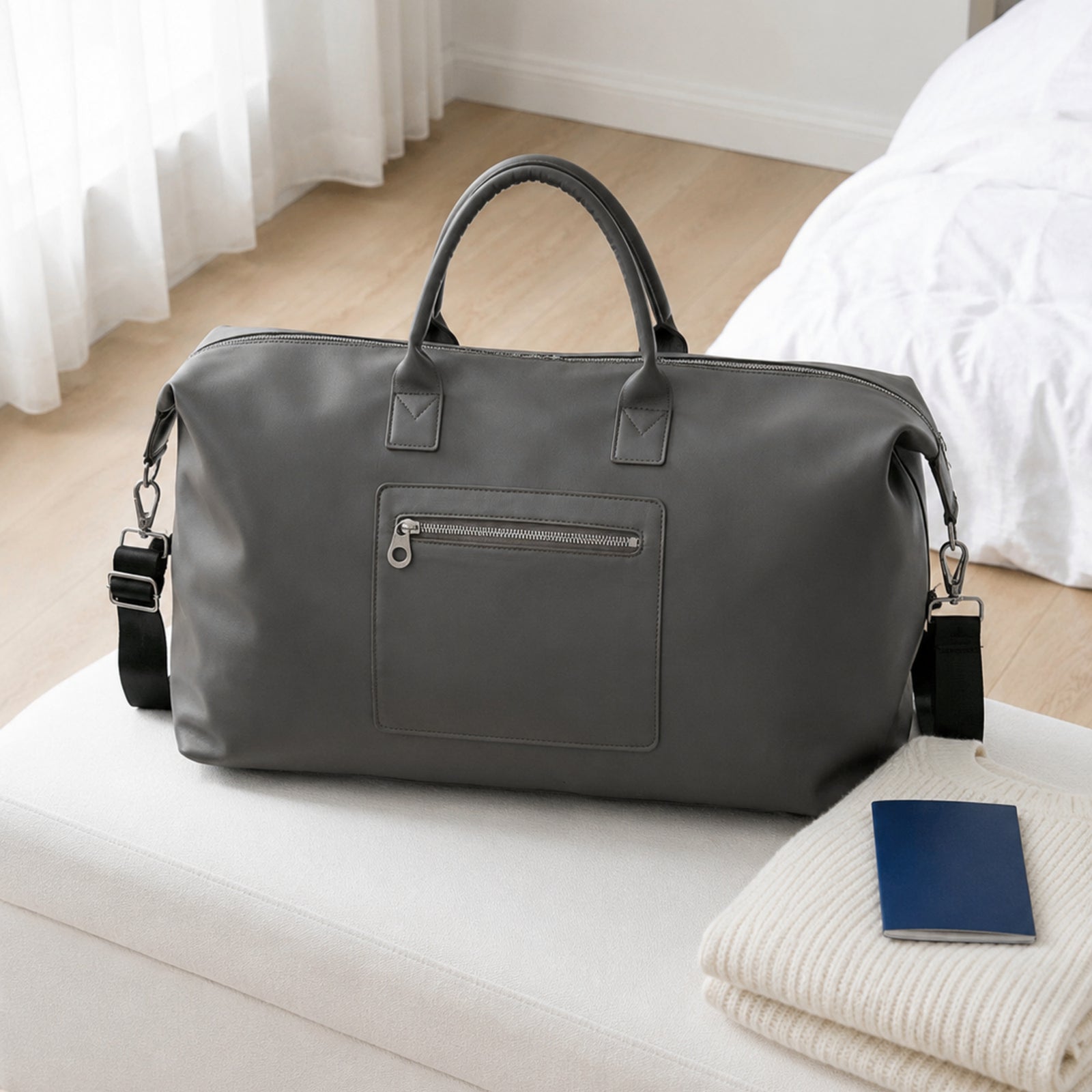 Gray Vegan PU Leather weekender on a white bedroom bench beside a blue passport cover