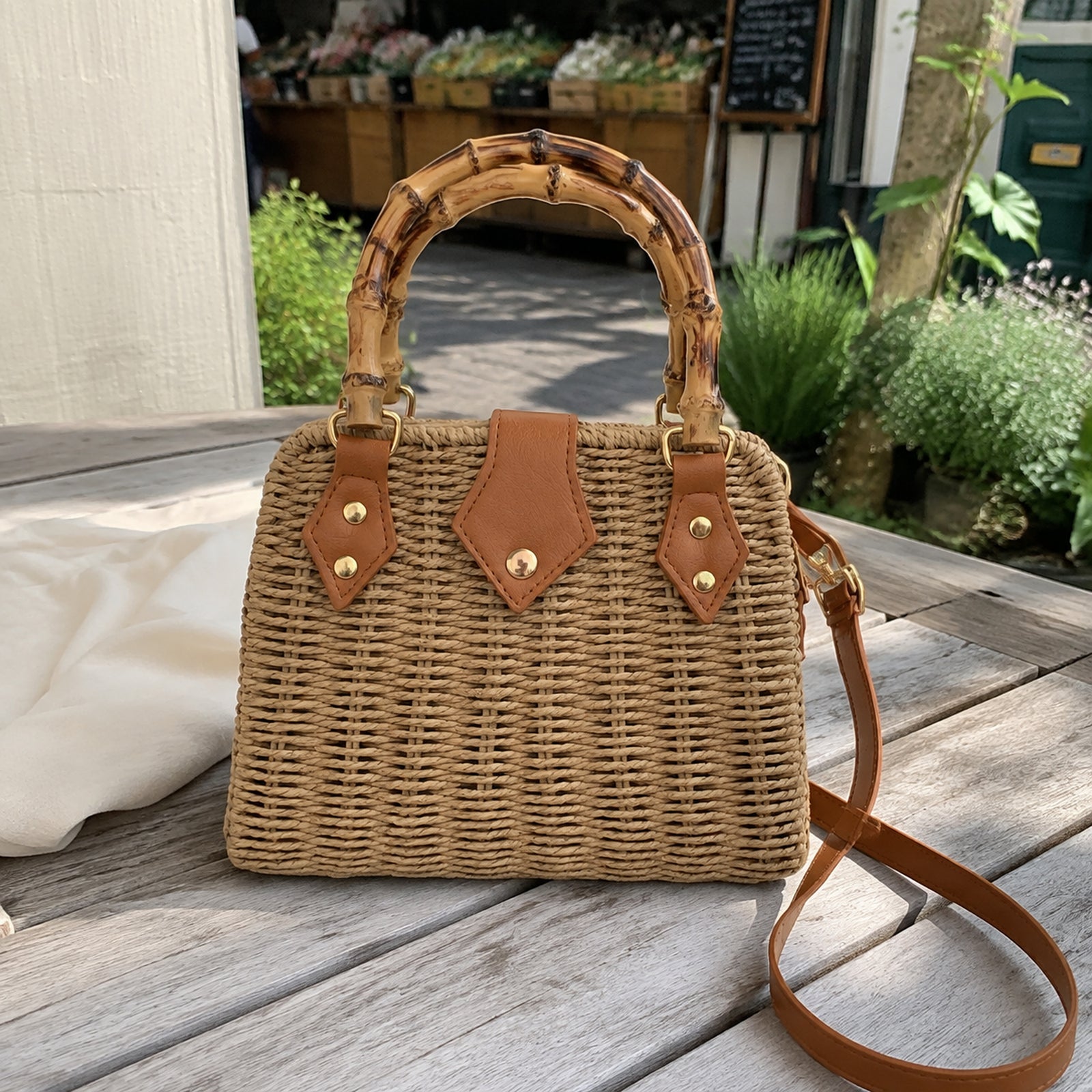 Khaki bamboo handle straw purse on a weathered wood table near a weekend market