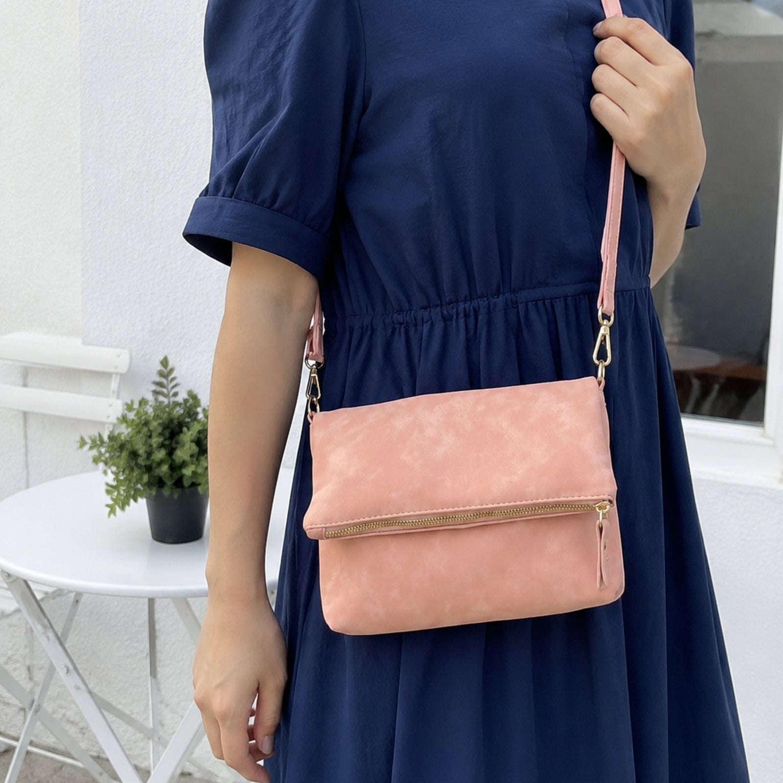 Blush pink envelope crossbody worn with a navy dress outside a bright cafe