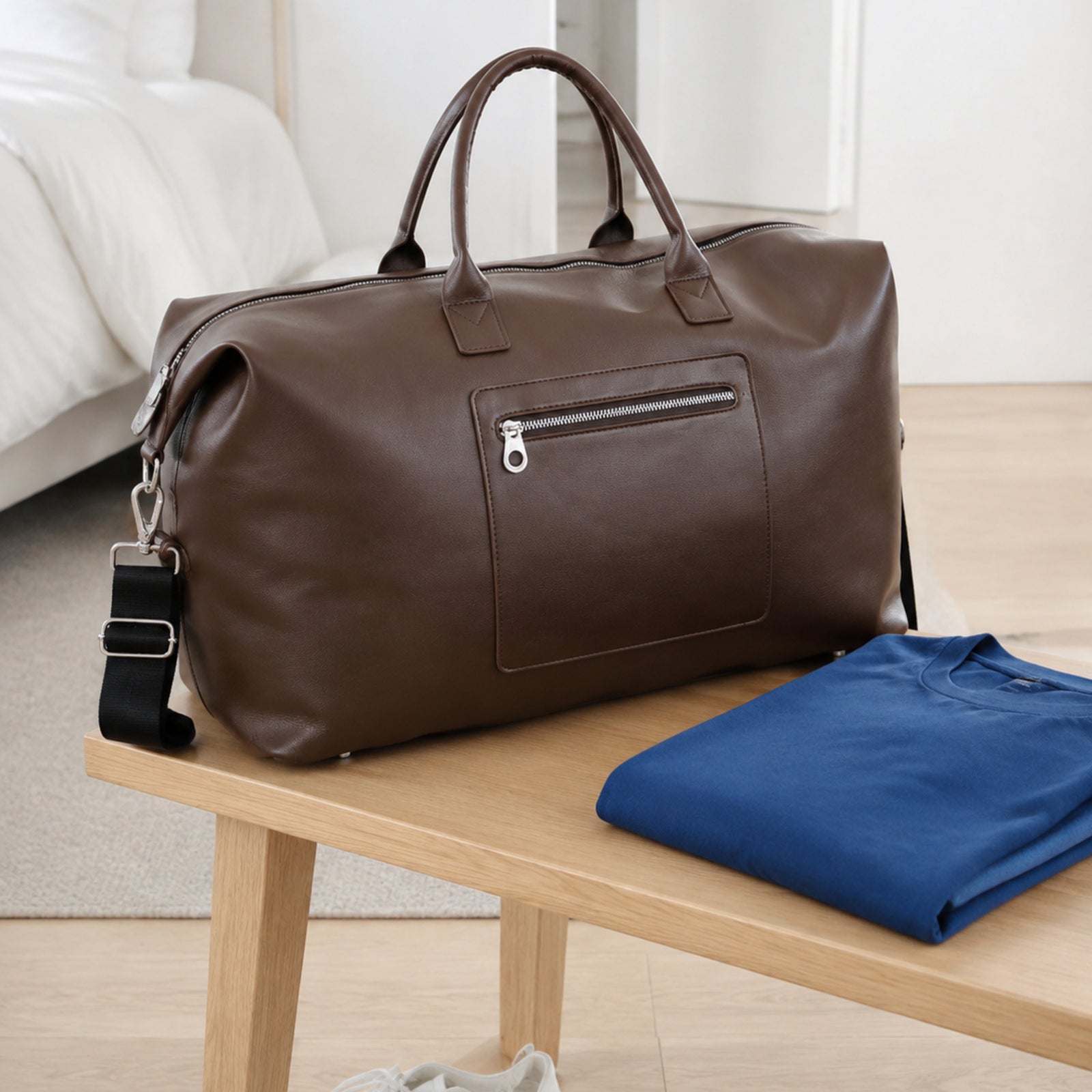 Brown large duffel bag styled with a folded blue shirt and white sneakers for a weekend trip