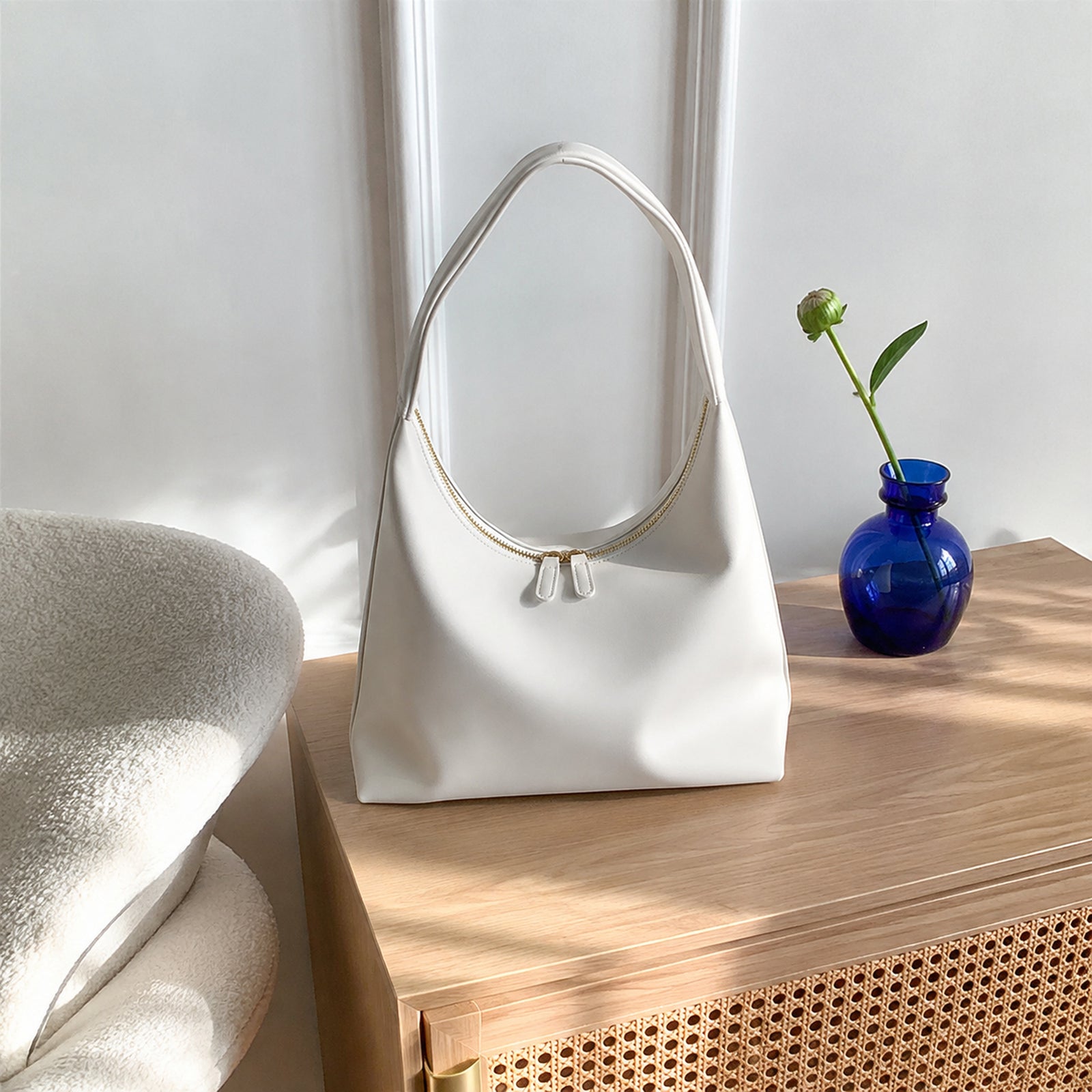 White Vegan PU Leather hobo bag on a pale oak console beside a cobalt blue vase