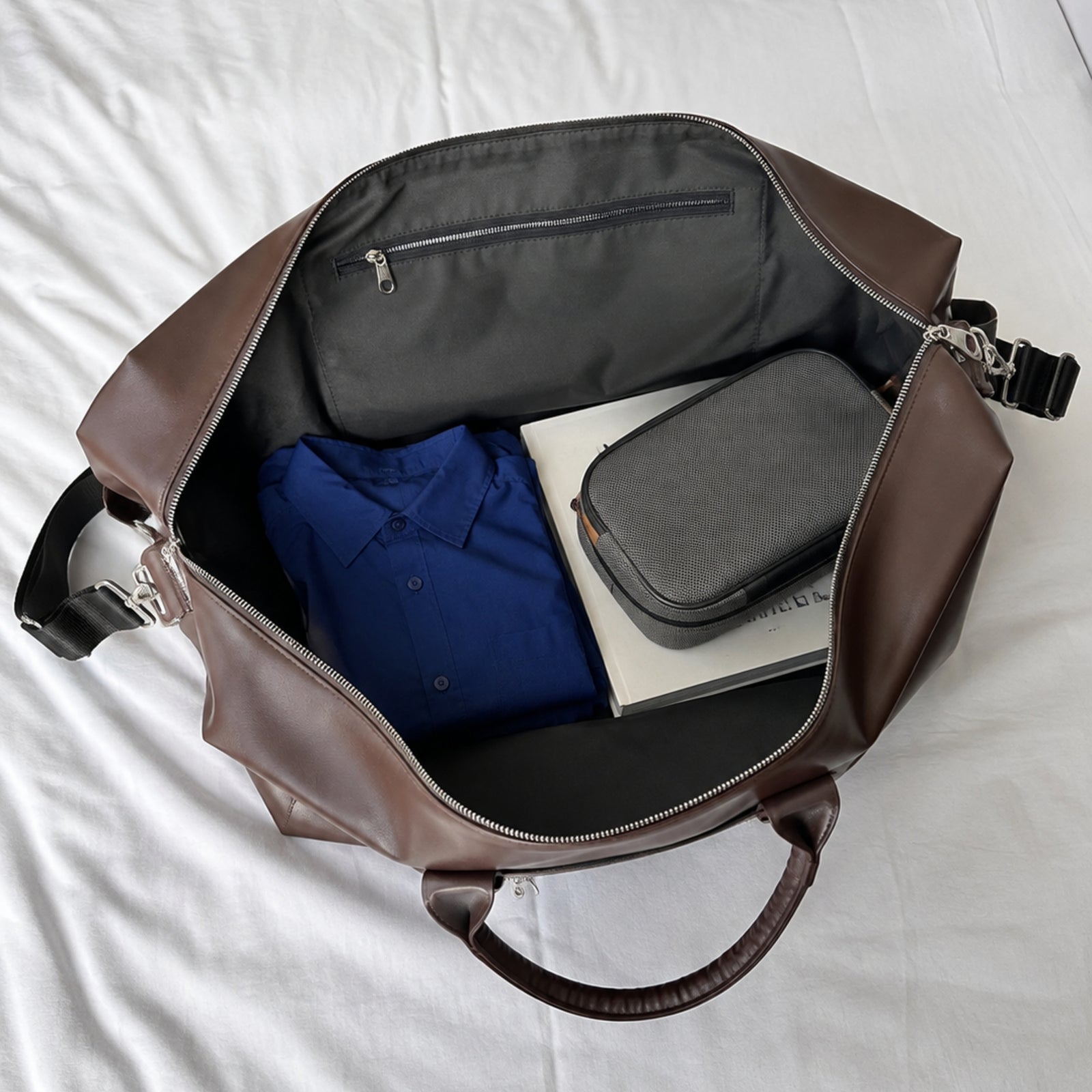 Open brown weekender showing roomy gray-lined interior, wall pocket, and packed essentials