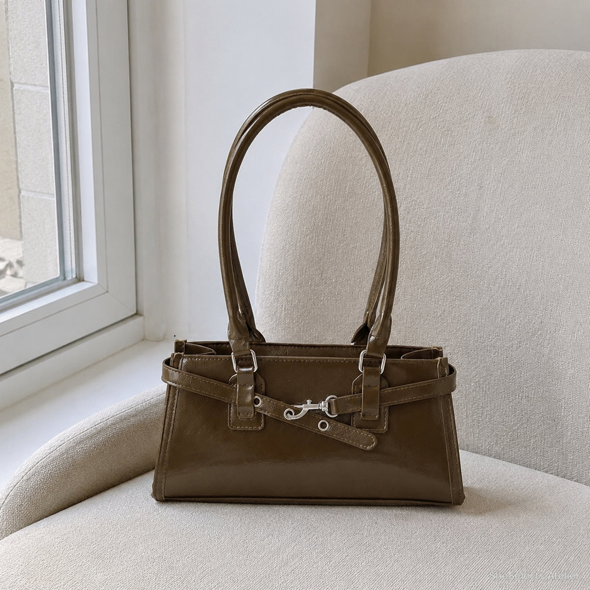 Khaki glossy baguette bag displayed on a cream chair