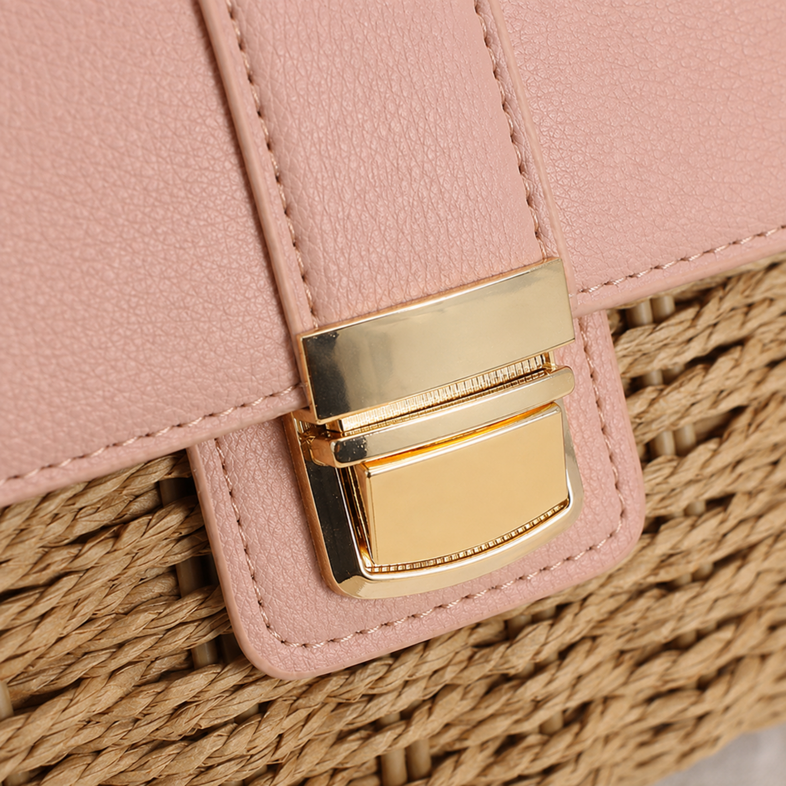 Close-up of gold push lock, pink vegan leather and straw weave