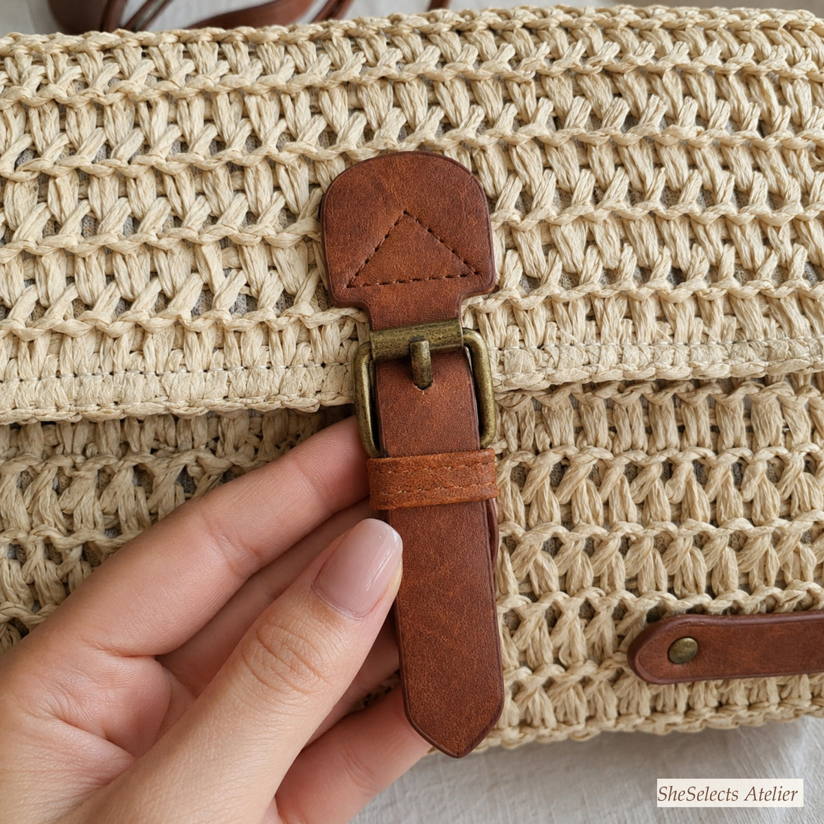 Close-up of brown buckle closure on a beige woven straw purse