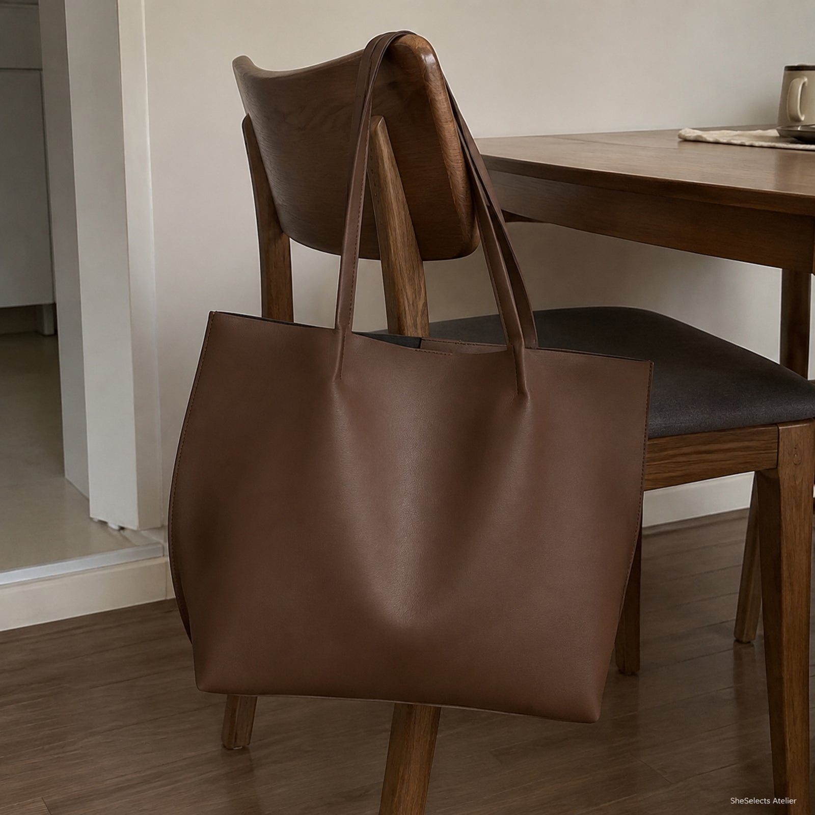 Side and back view of the coffee brown open-top tote hanging naturally from a wooden chair
