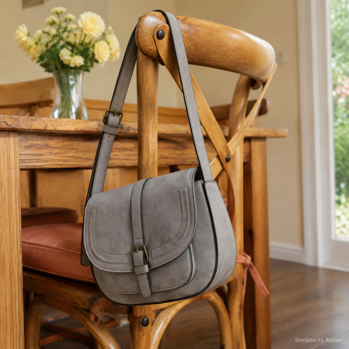 Three-quarter side view of a grey vintage saddle bag hanging on a wooden chair