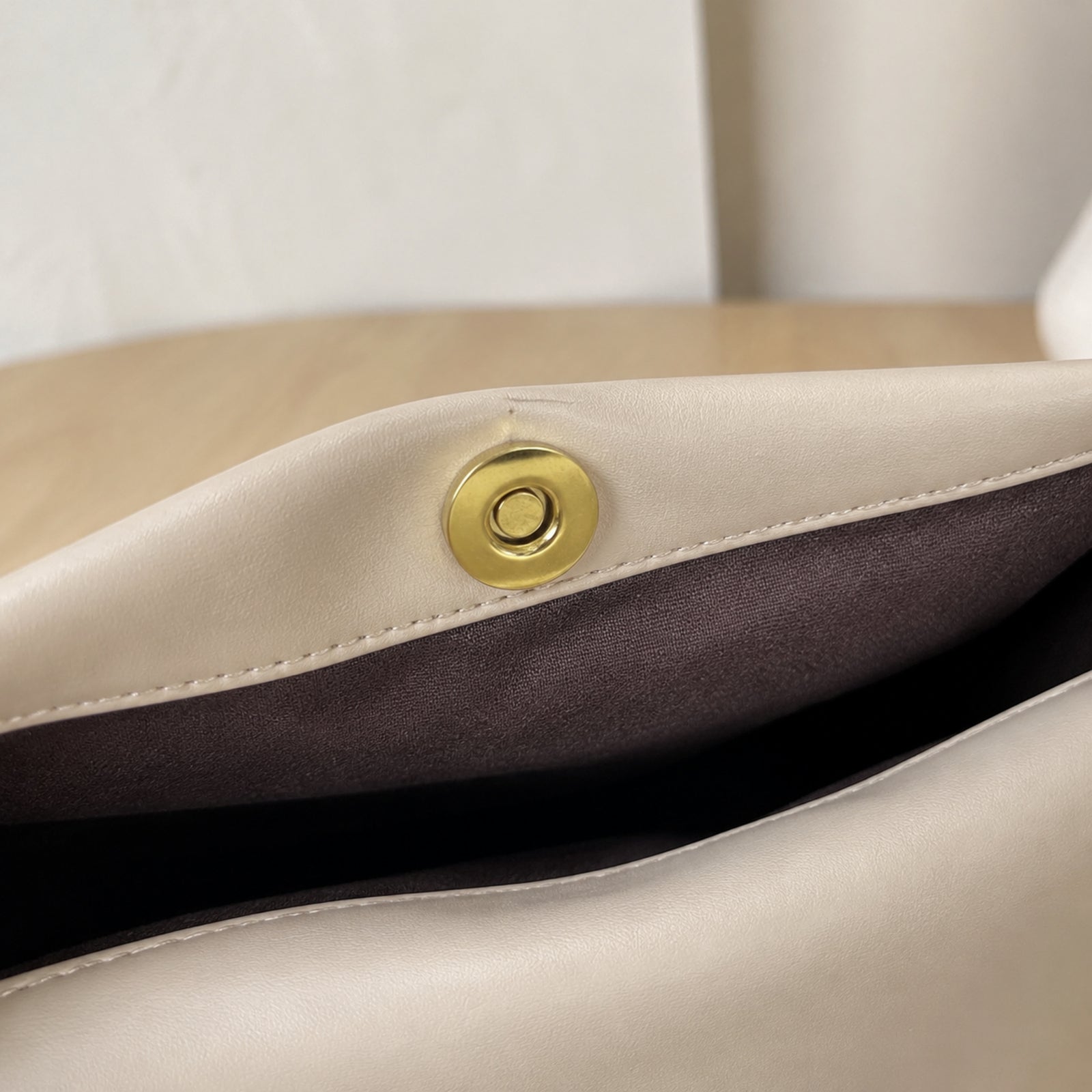 Close view of the gold-tone magnetic snap and dark lining inside the beige tote