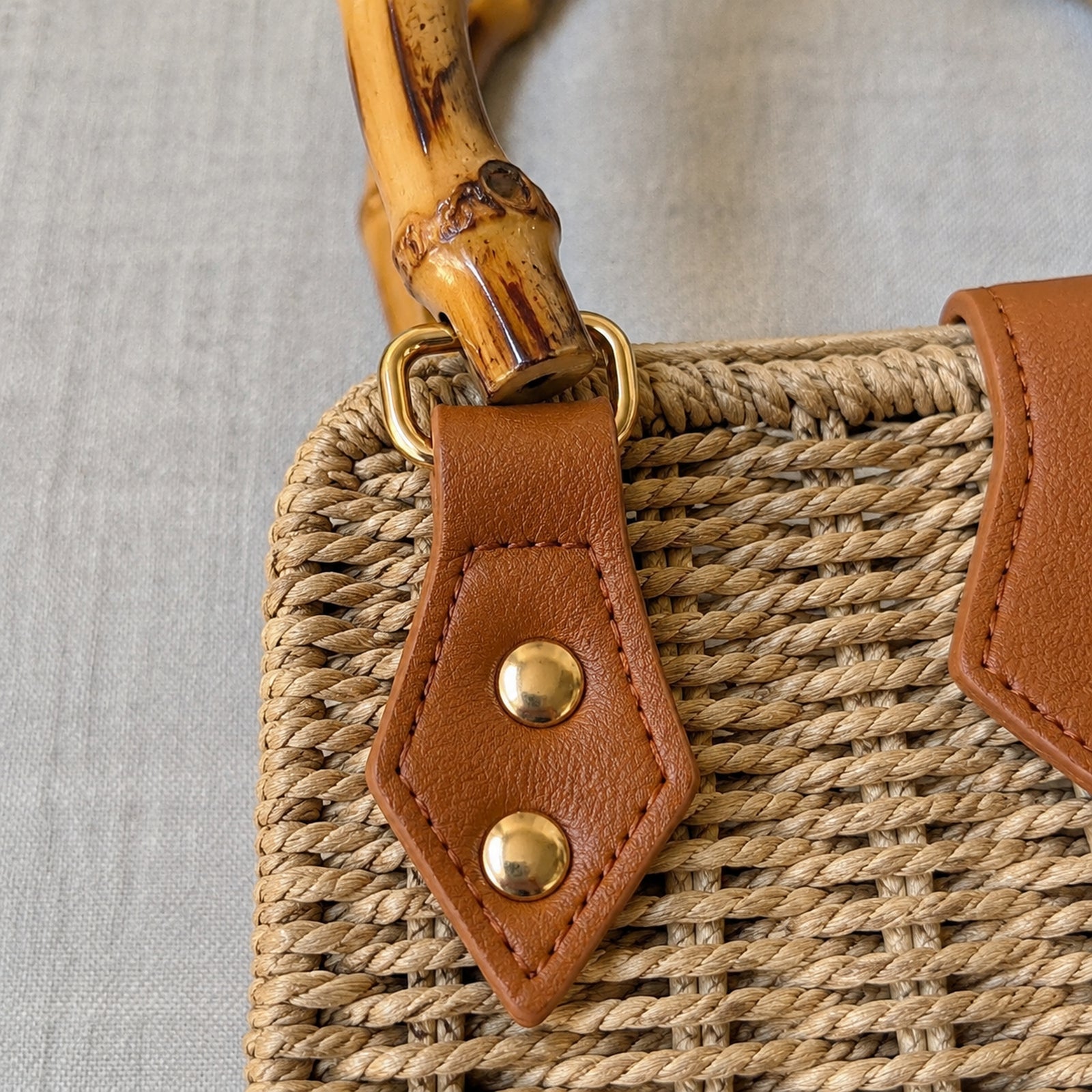 Close-up of bamboo handle, tan Vegan PU Leather tab, gold rivets, and woven straw texture