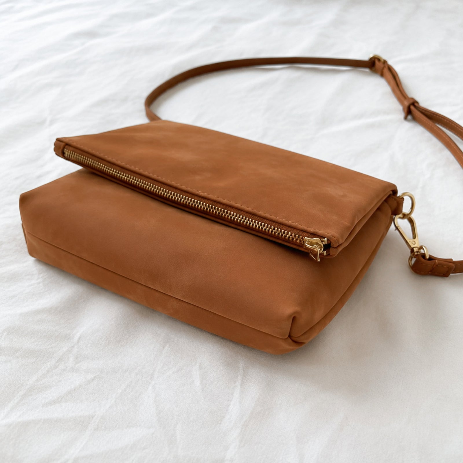 Brown envelope crossbody shown from the side with foldover flap, base, and adjustable strap