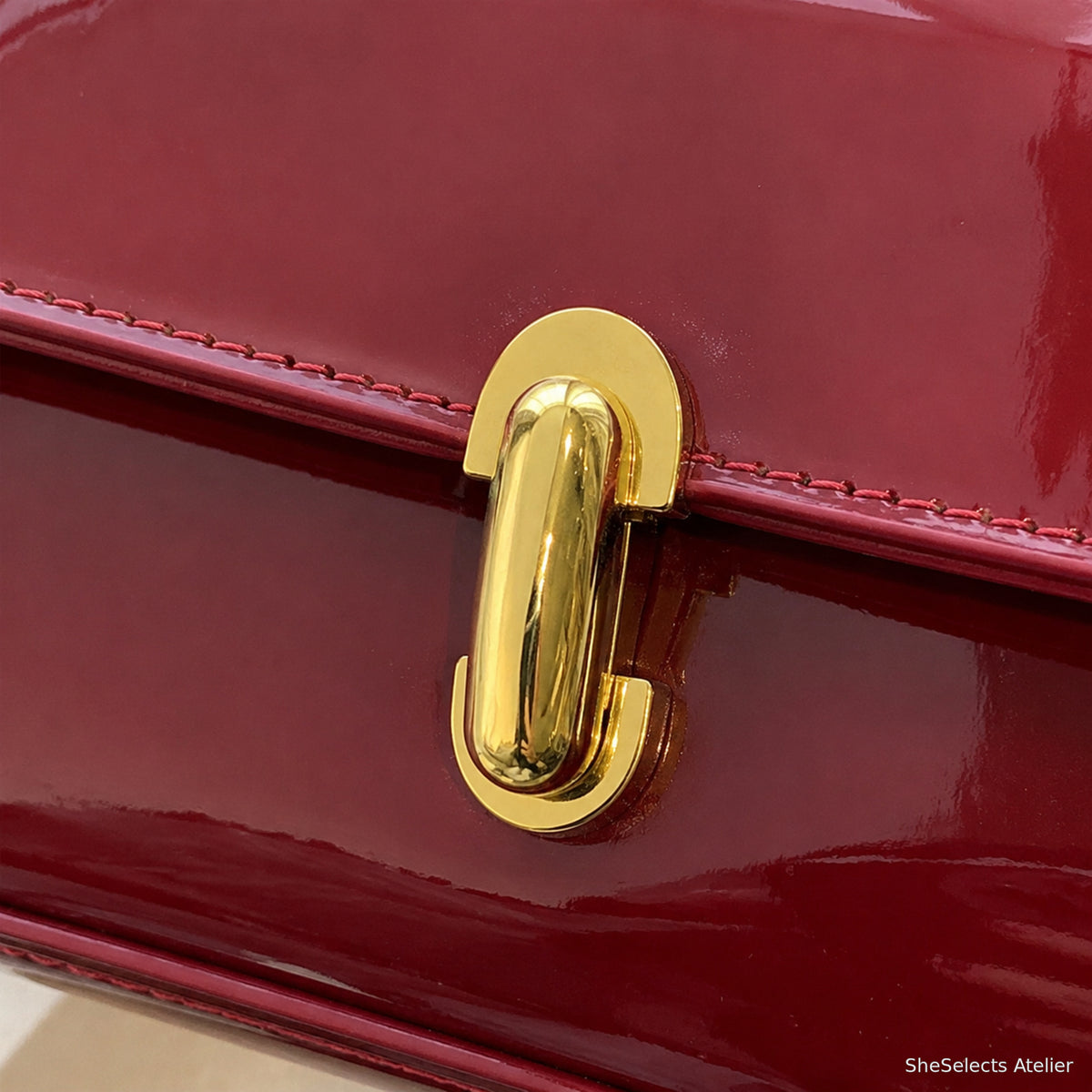 Close-up of gold rotating turn-lock on Wine Red glossy shoulder bag