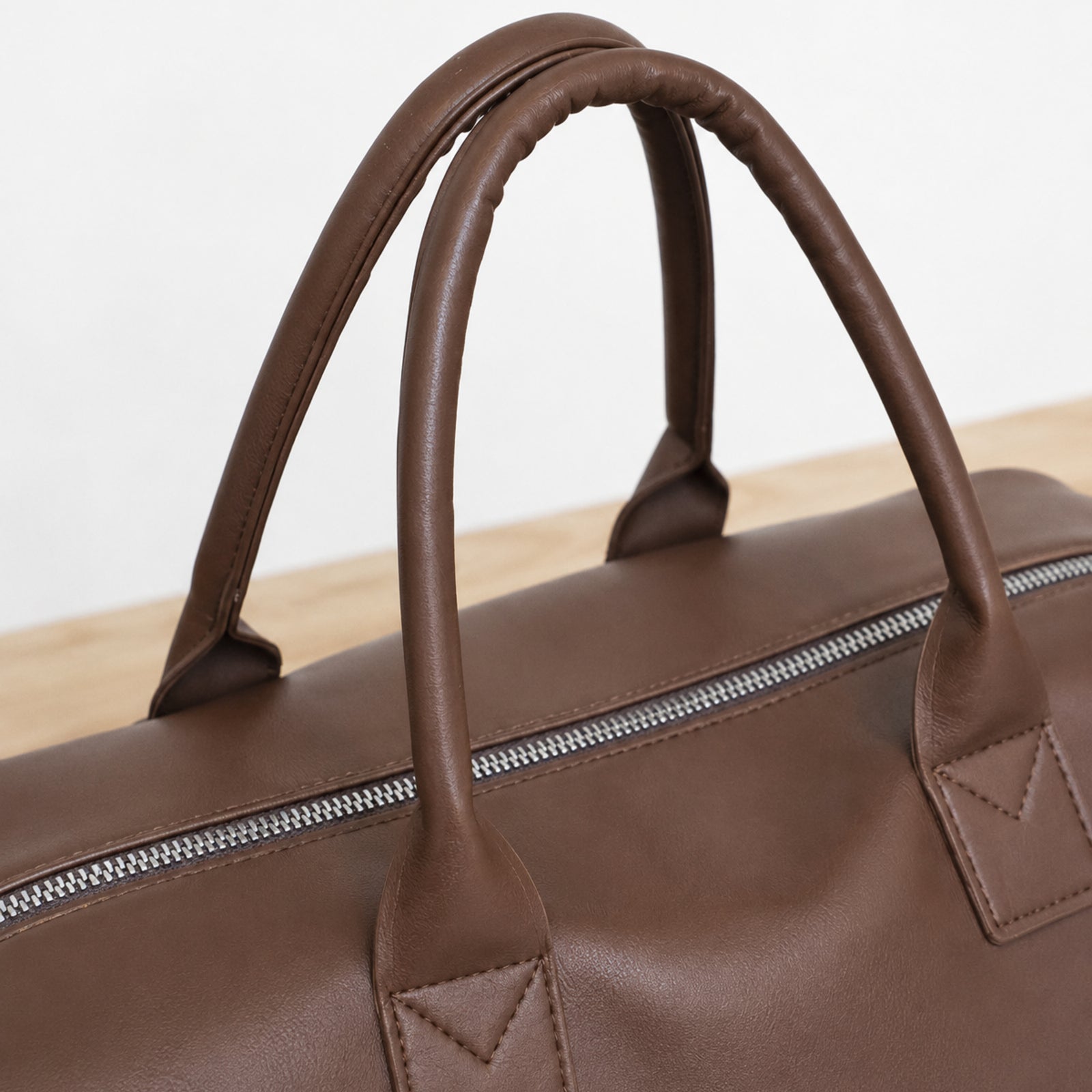 Close view of brown padded handles, reinforced tabs, and silver top zipper track