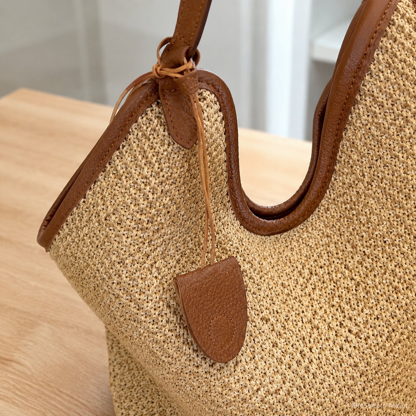 Close-up of brown tote strap attachment, stitched edge, cord, and hanging tag