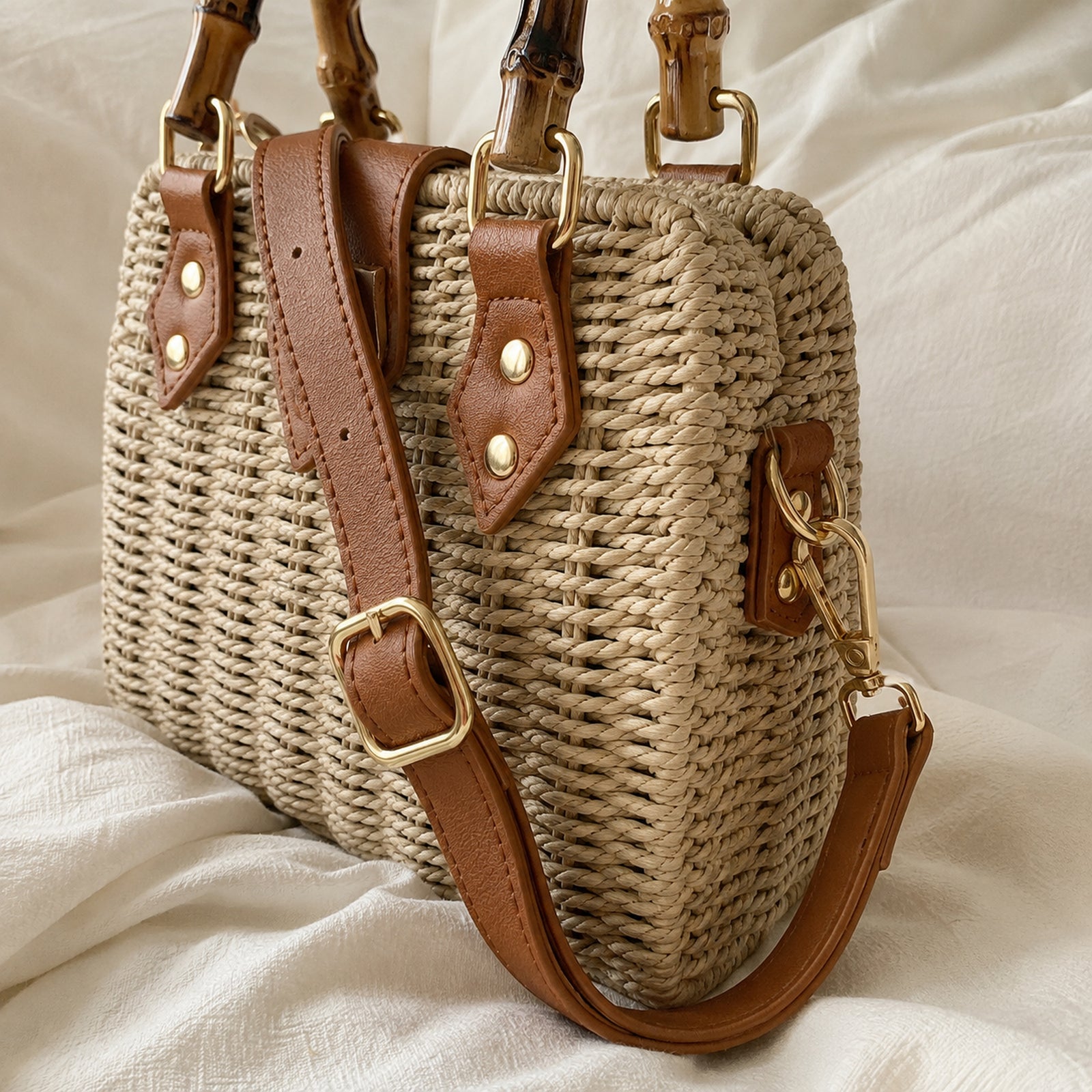 Close-up of adjustable tan shoulder strap, gold buckle, side hook, and woven bag edge