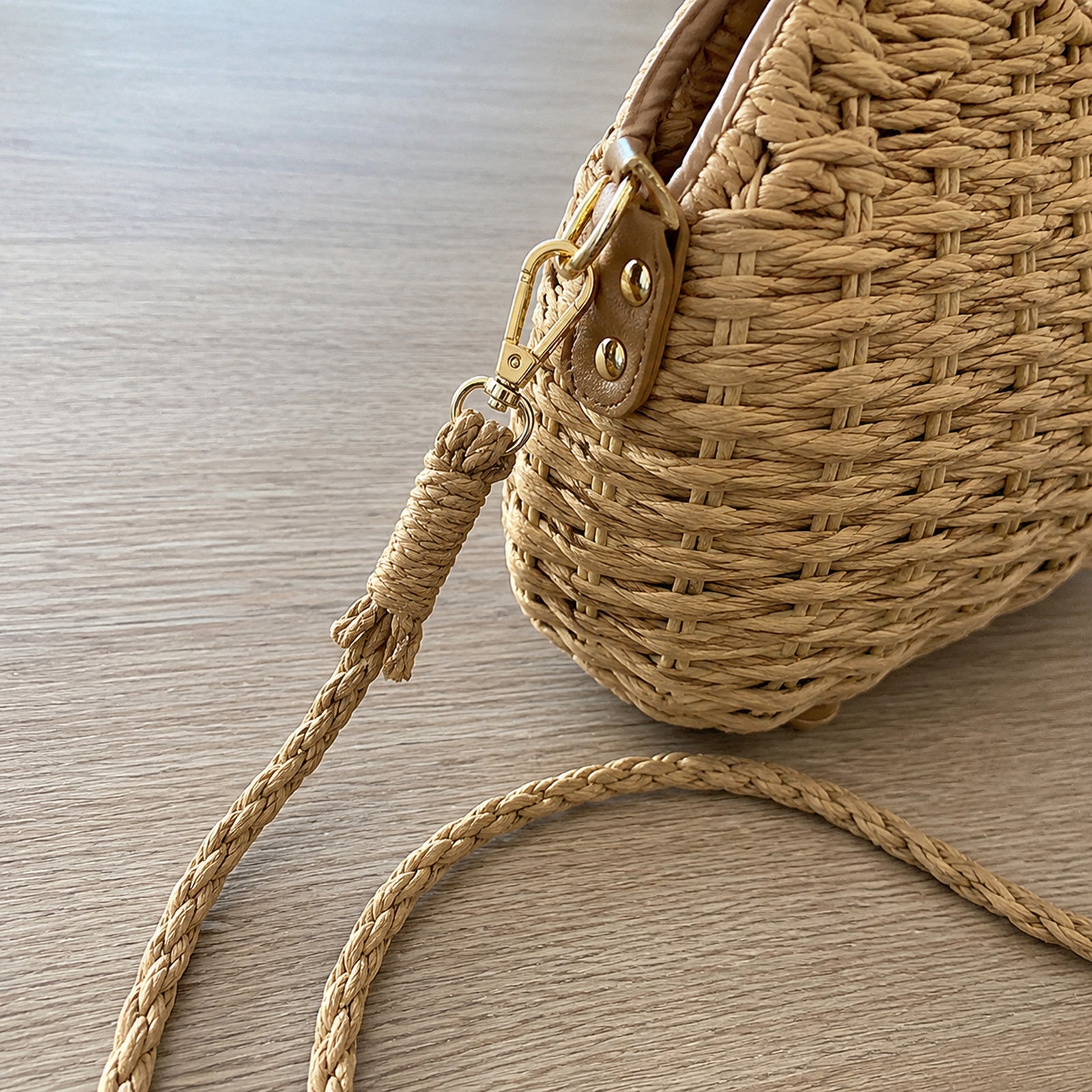 Close-up of braided shoulder strap, gold clasp, side attachment, and woven bag texture
