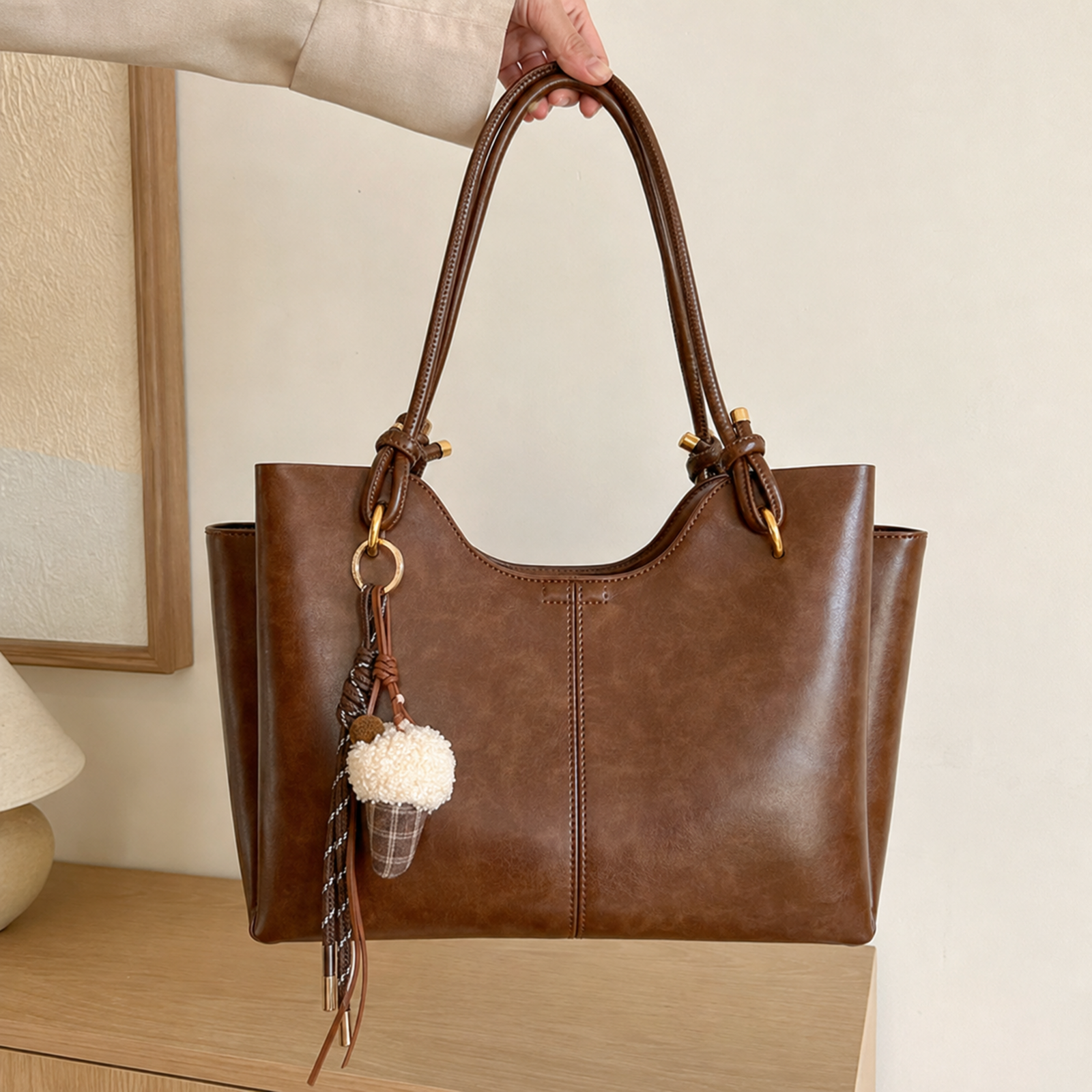 Brown work tote with pompom charm held by the top handles