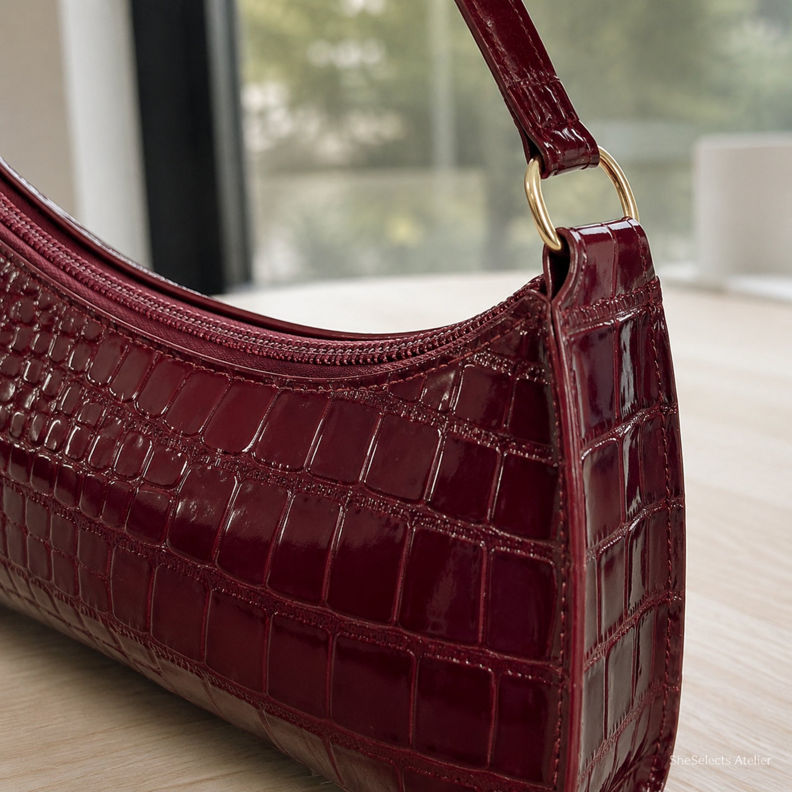 Close-up of wine red croc embossing, curved zipper, stitching, strap, and metal ring