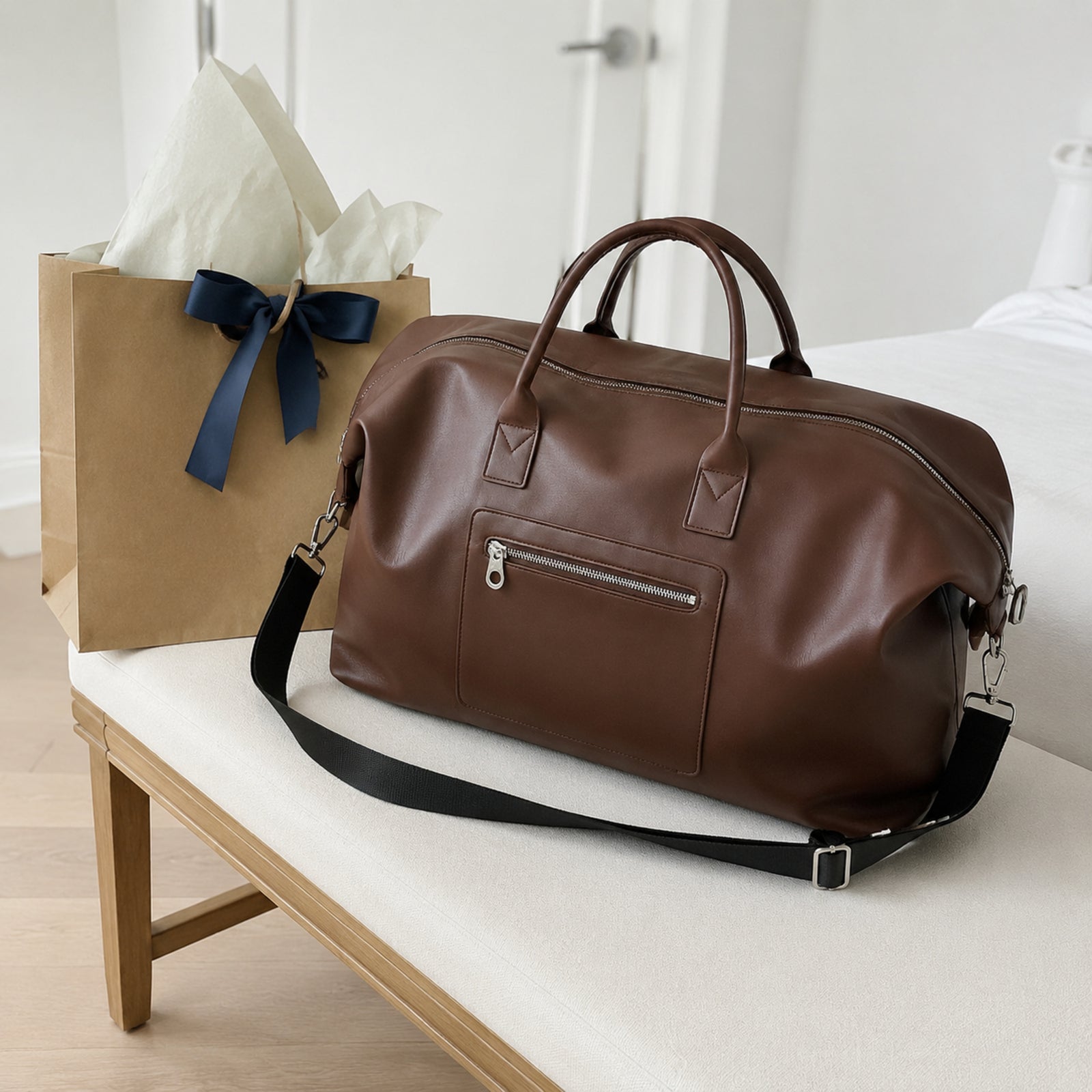 Brown large weekender bag styled beside kraft gift packaging with blue ribbon