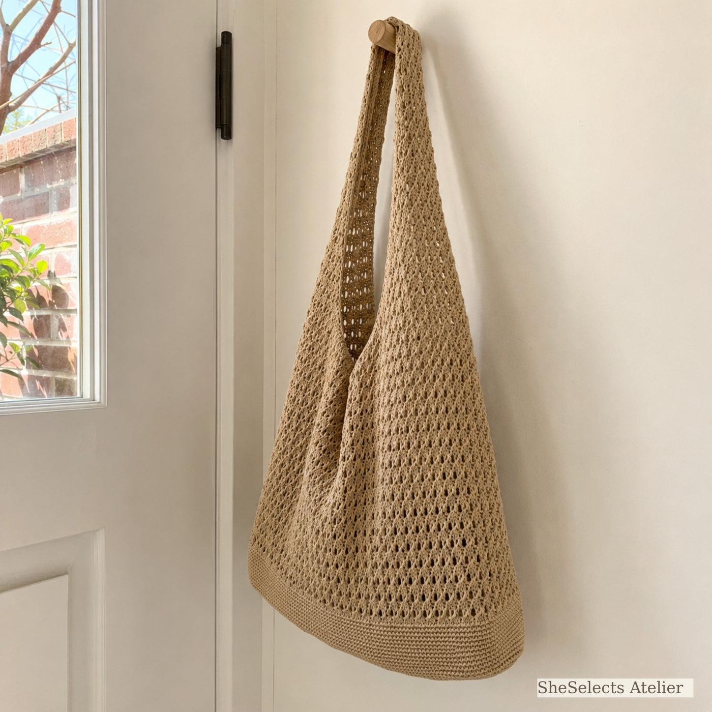 Side view of khaki crochet style market tote hanging by a door