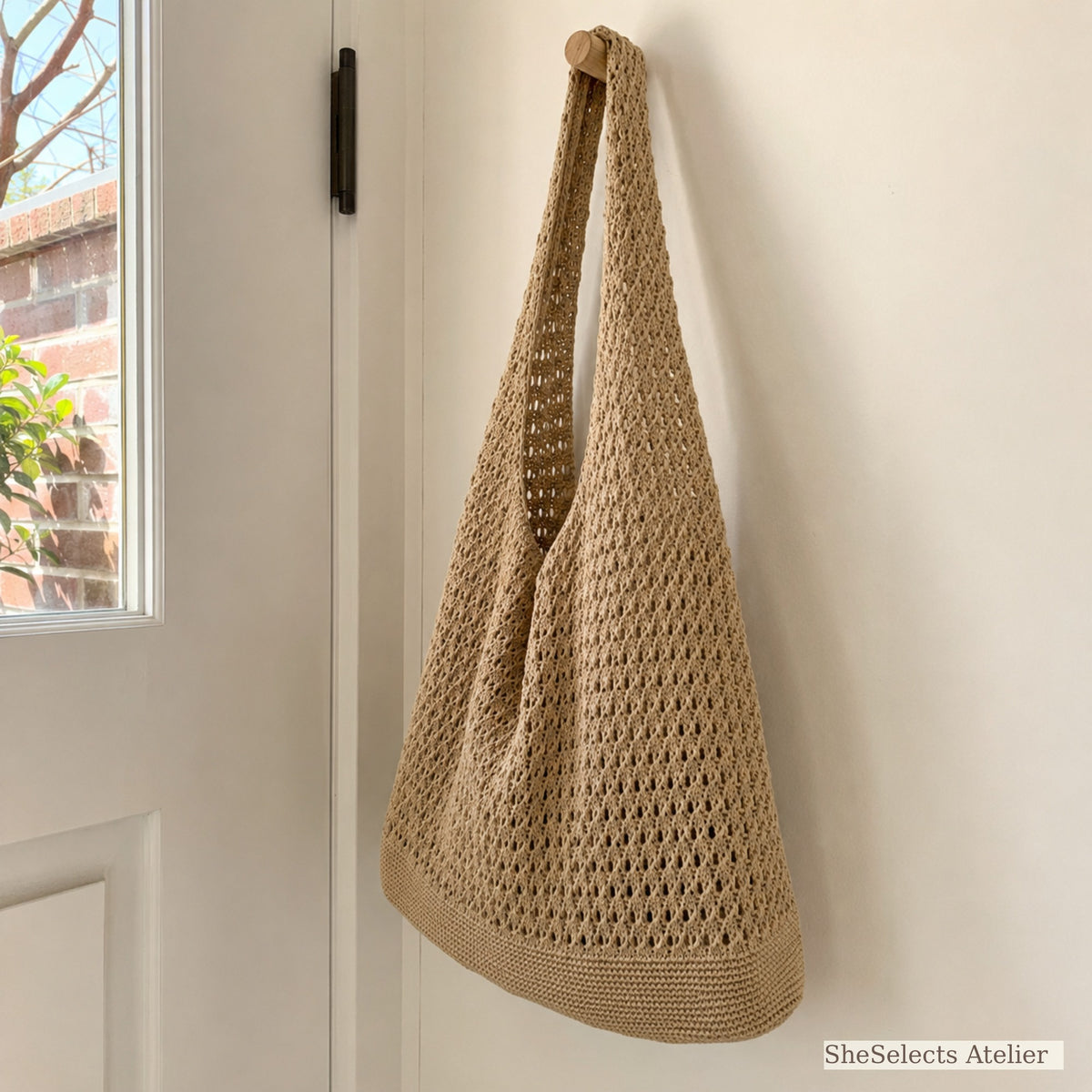 Side view of khaki crochet style market tote hanging by a door
