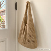Side view of khaki crochet style market tote hanging by a door