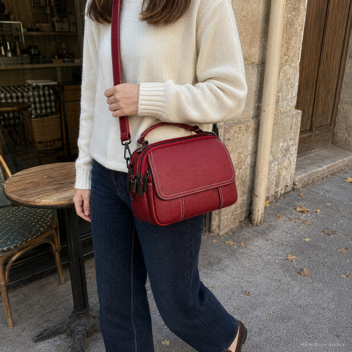 Wine Red genuine leather crossbody bag worn with cream knit and dark denim outside a cafe