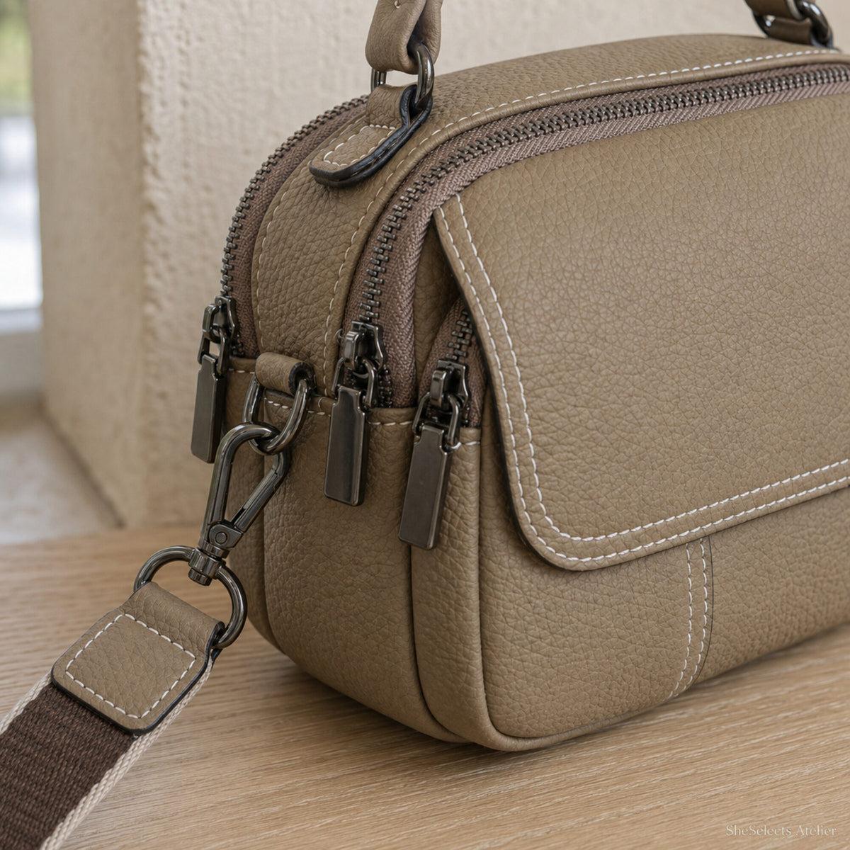 Khaki pebbled leather crossbody bag close up showing white stitching zippers and strap hardware
