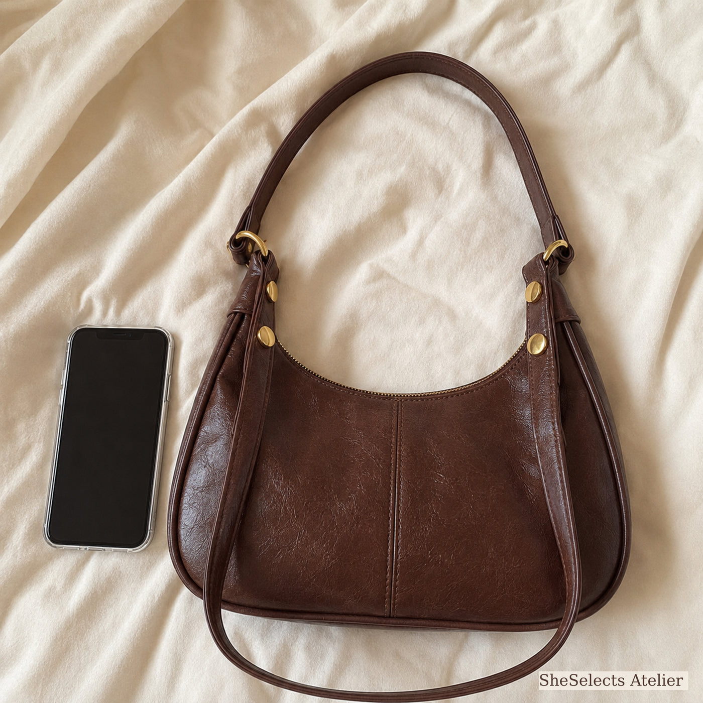 Brown crescent shoulder bag beside a smartphone for everyday scale reference