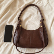 Brown crescent shoulder bag beside a smartphone for everyday scale reference