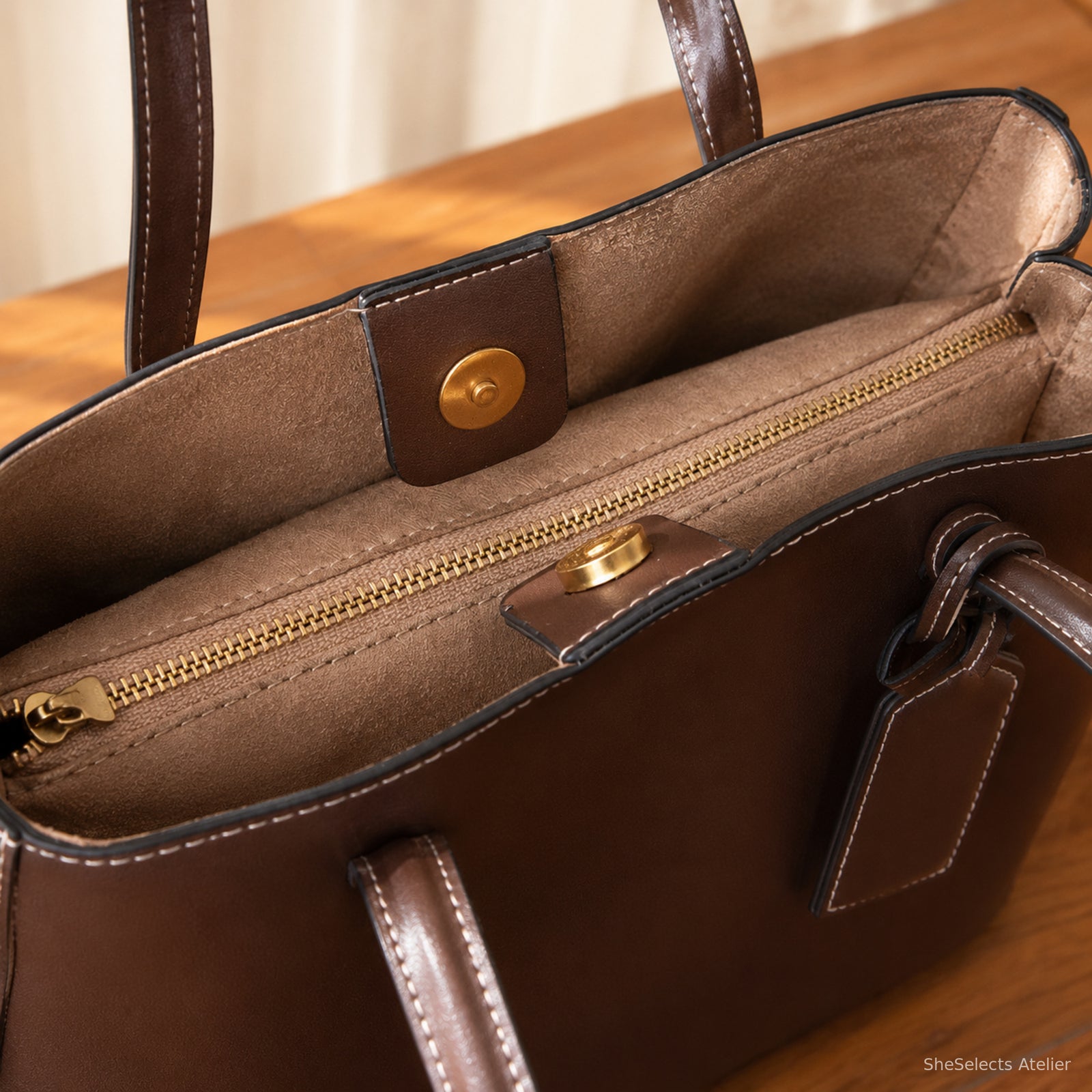 Close-up of brown tote magnetic snap tabs, tan lining, and gold zipper