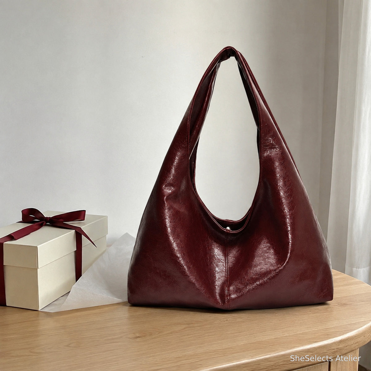 Wine red slouchy shoulder bag styled beside a simple ribbon gift box