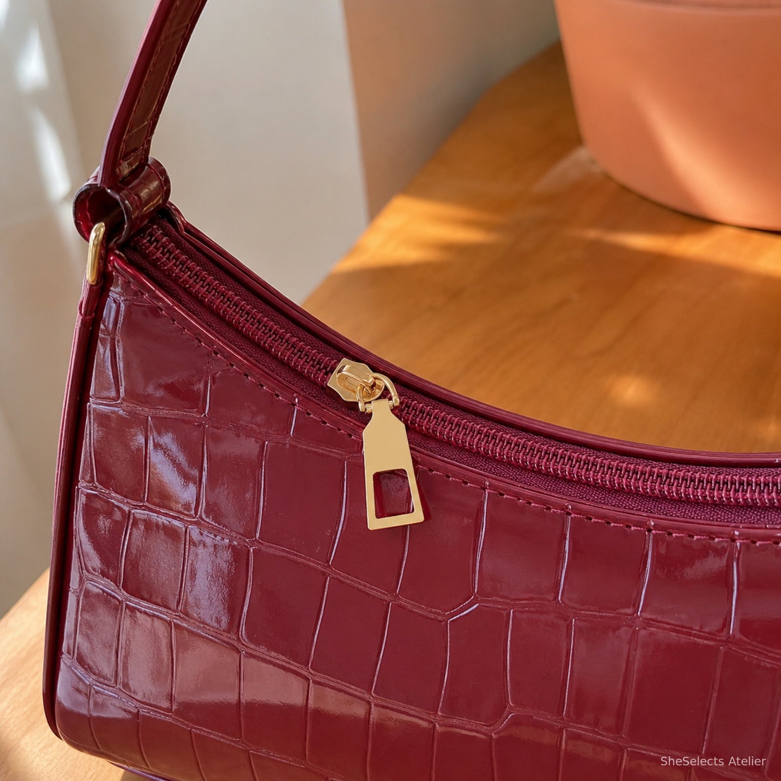 Close-up of wine red croc bag curved zipper and gold rectangular pull