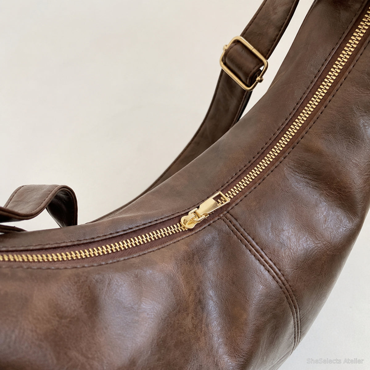 Close view of the dark brown bag's gold top zipper and stitched panel seam