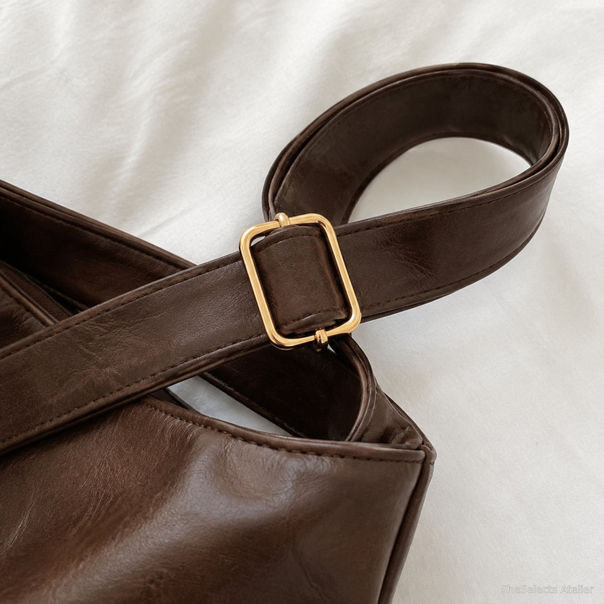 Close view of the brown adjustable shoulder strap, gold buckle and edge stitching