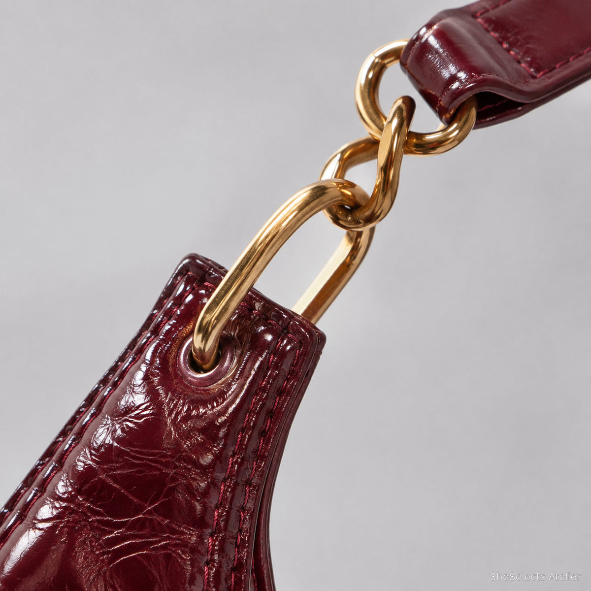Gold chain and burgundy shoulder strap connection close up