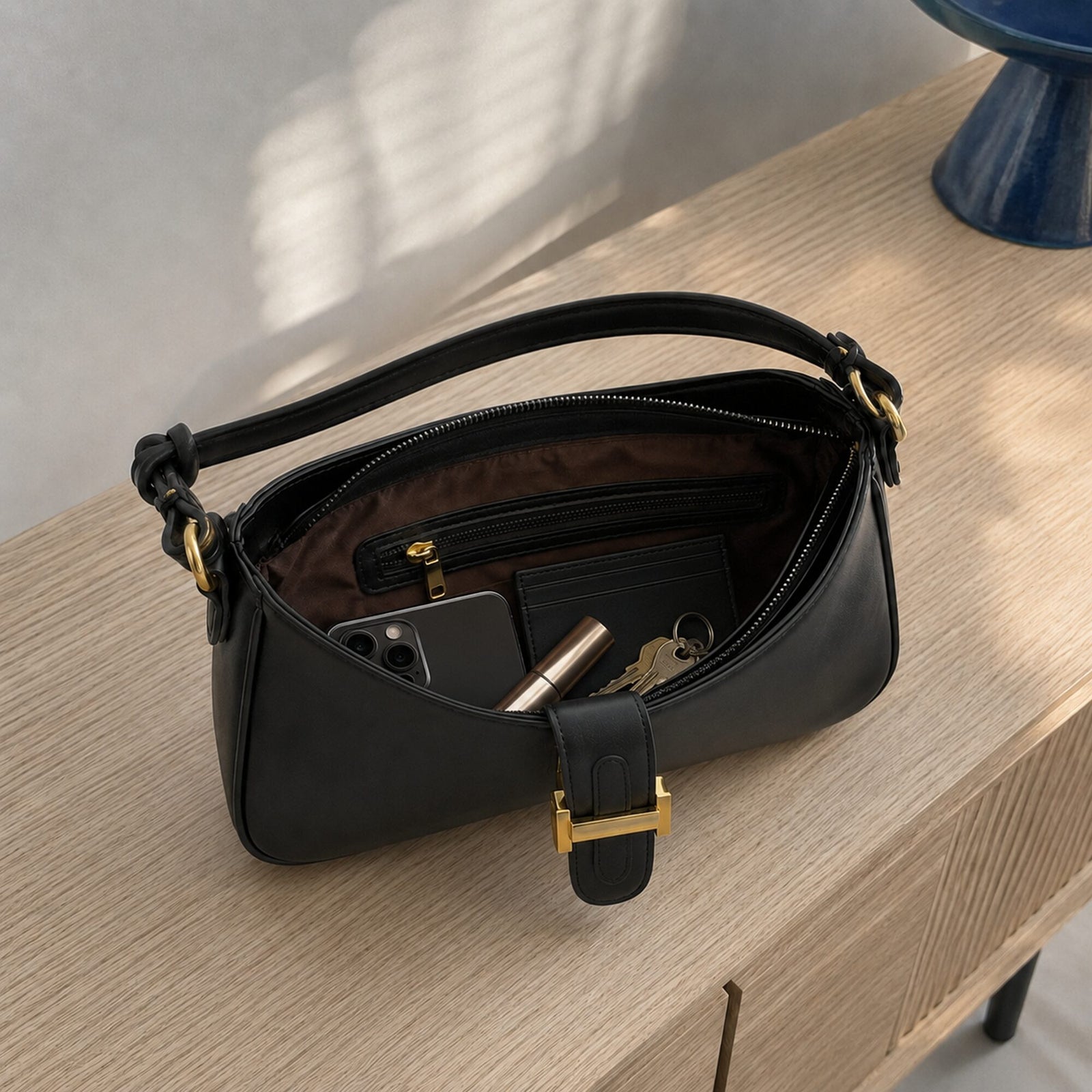 Black vegan leather baguette bag opened with phone, cardholder, keys and lipstick