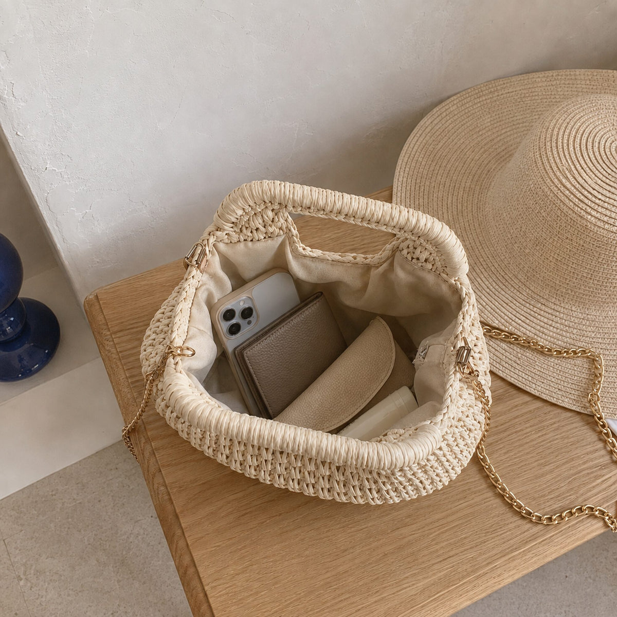 Cream oval-handle woven straw bag opened with phone, wallet, sunglasses case and sunscreen