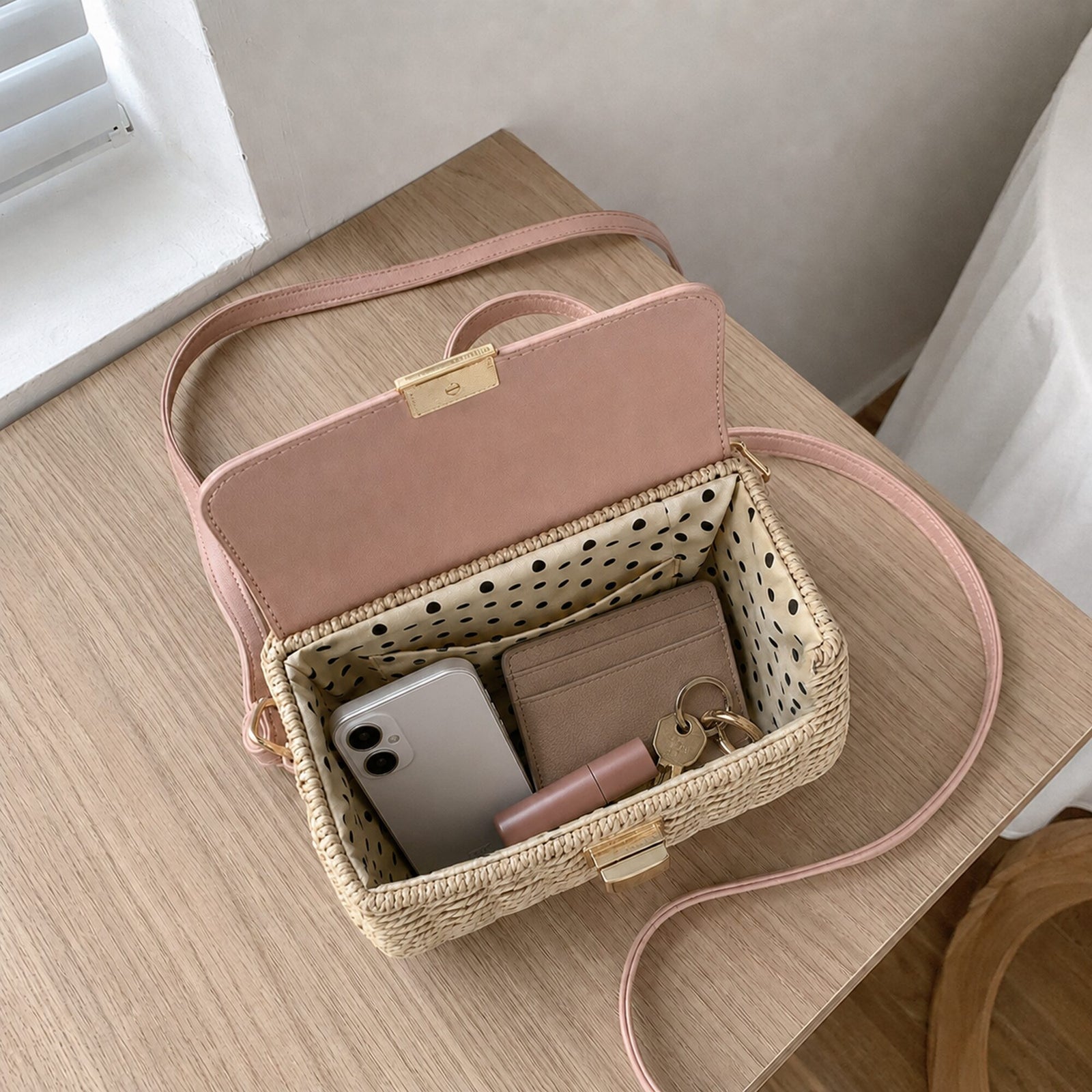 Blush-flap woven straw satchel opened with phone, cardholder, keys and lipstick