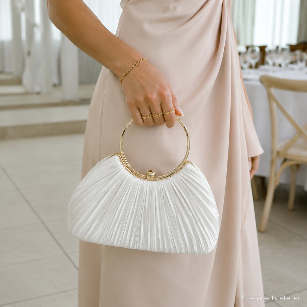 White pleated satin ring handle clutch styled with a wedding guest dress