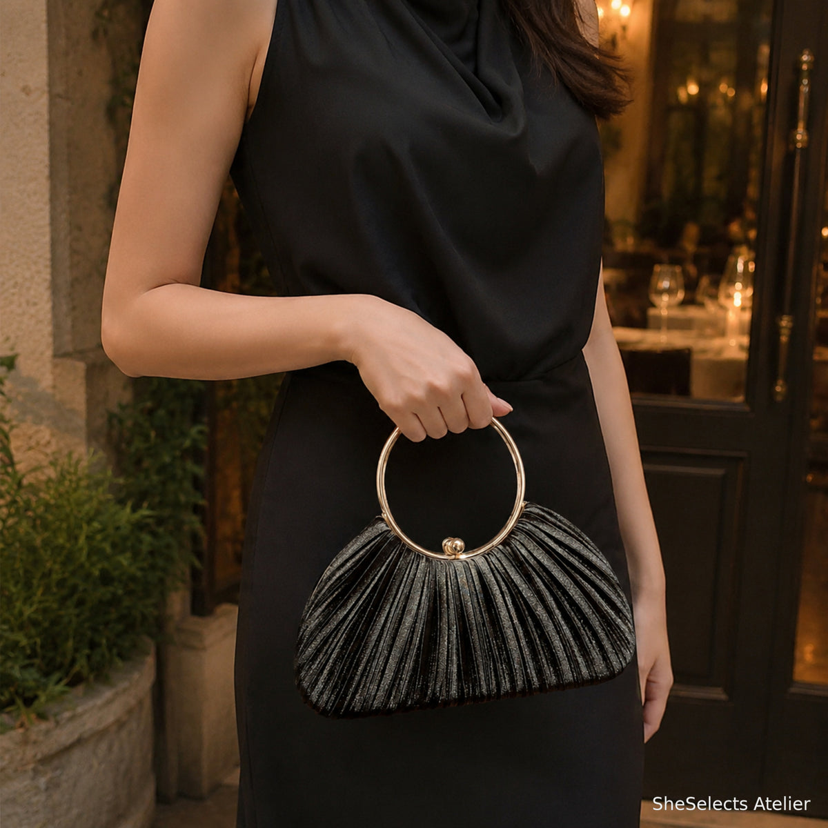 Black pleated satin ring handle evening bag held with a formal black outfit