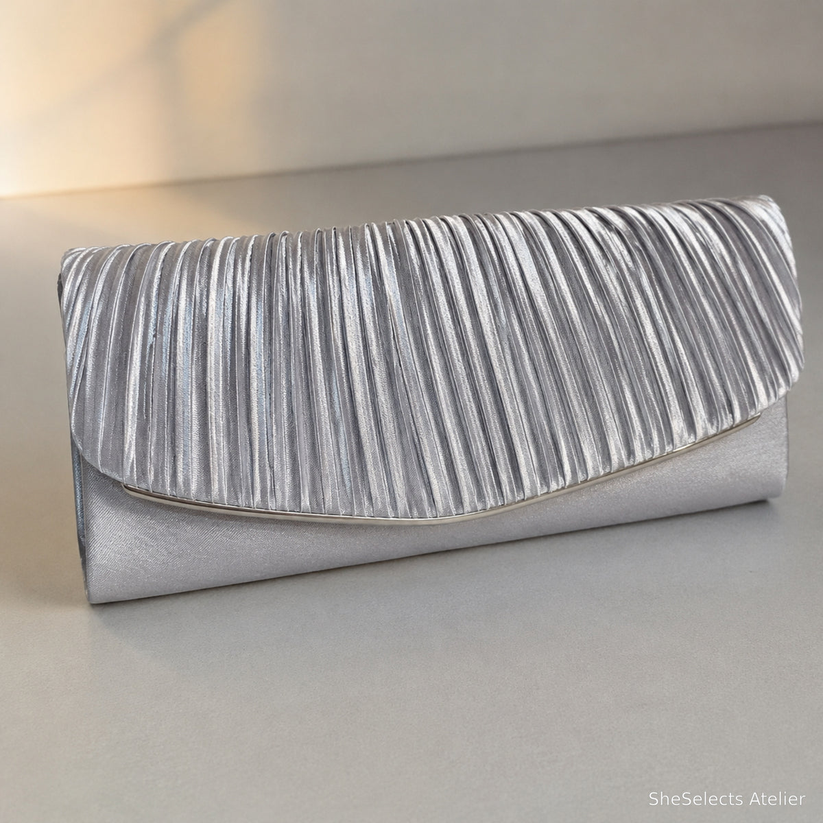 Silver pleated satin envelope evening clutch on a cool gray surface